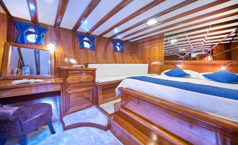 Stella Maris cabin interior with polished wood paneling, blue accents, and a large bed