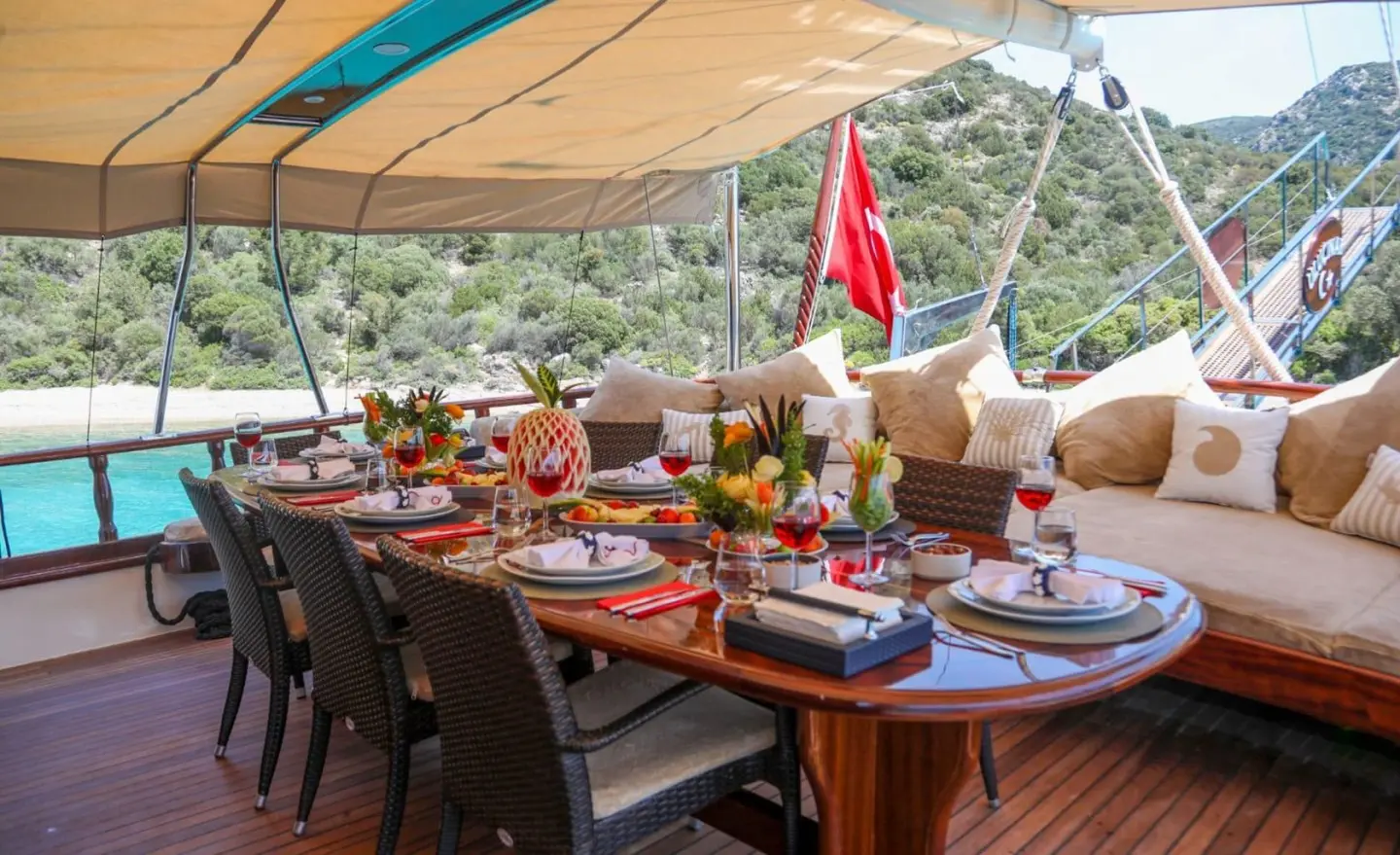 A gulet aft deck setup with seating, tableware, and sea view under a canopy