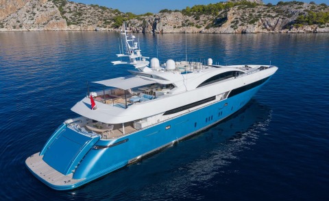 White and blue luxury yacht seen from an angled rear-side view on calm blue sea