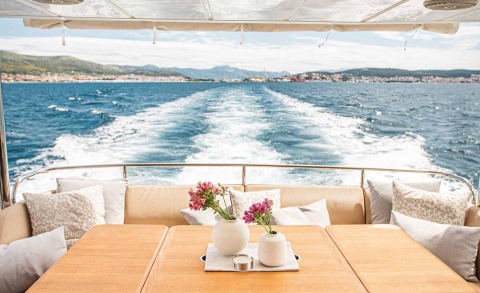 View from the yacht's aft deck toward the sea with wake behind, foreground shows table and cushions with floral vases