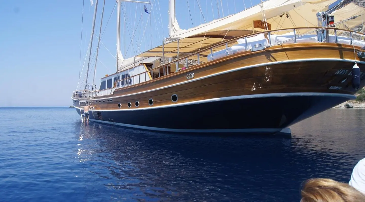 Kaya Guneri 5 yacht sailing at dusk with dark blue hull and wooden upper decks