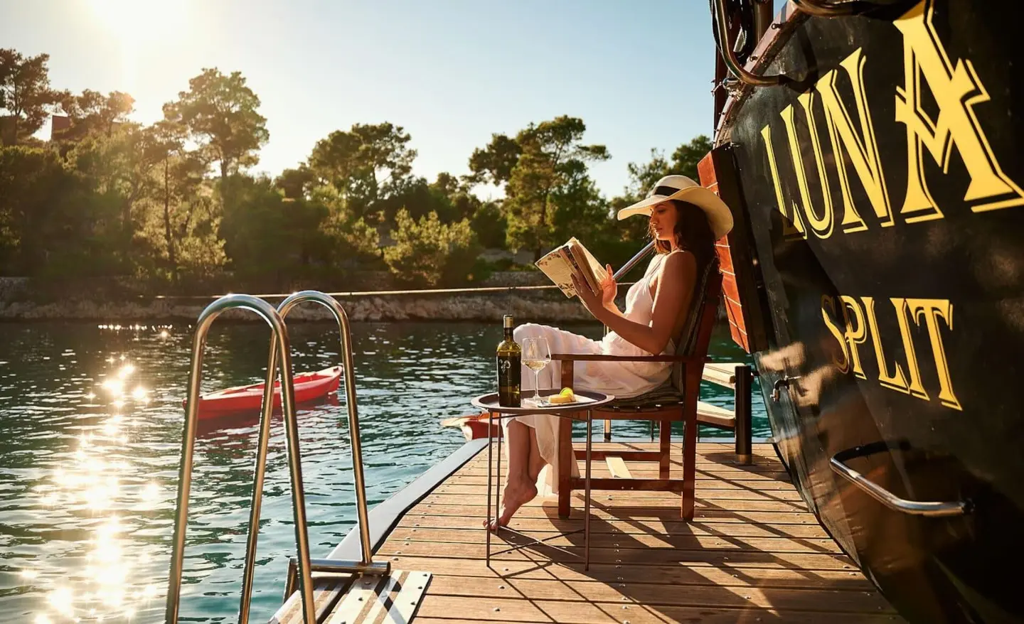 Luna yacht on calm water at sunset with passengers on wooden deck railing