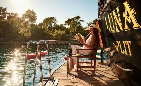 Luna yacht docked with woman in sunhat reading onboard a deck chair by the water