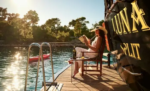 Luna yacht on calm water at sunset with passengers on wooden deck railing