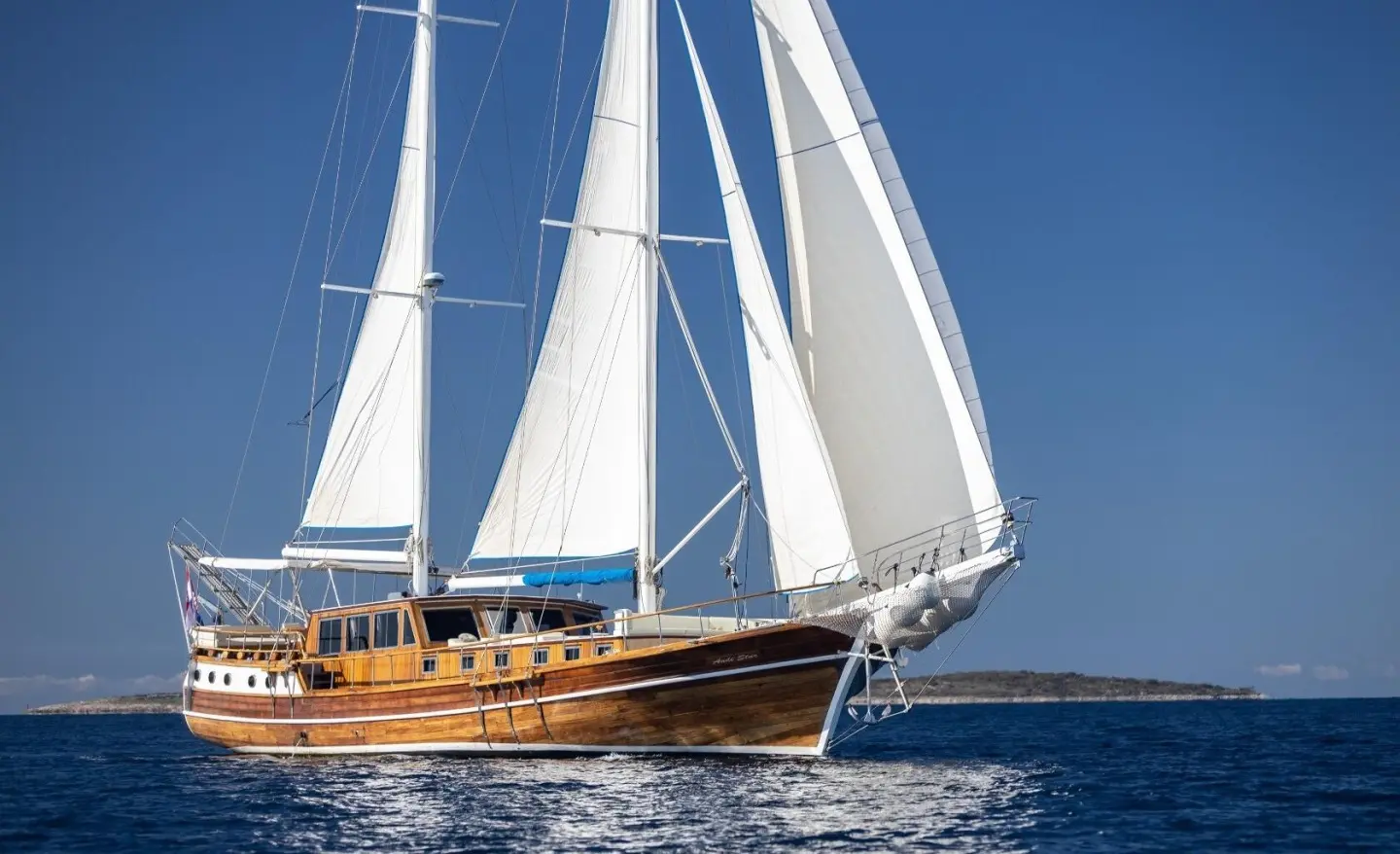 Large wooden-hulled sailing yacht on blue sea with clear sky
