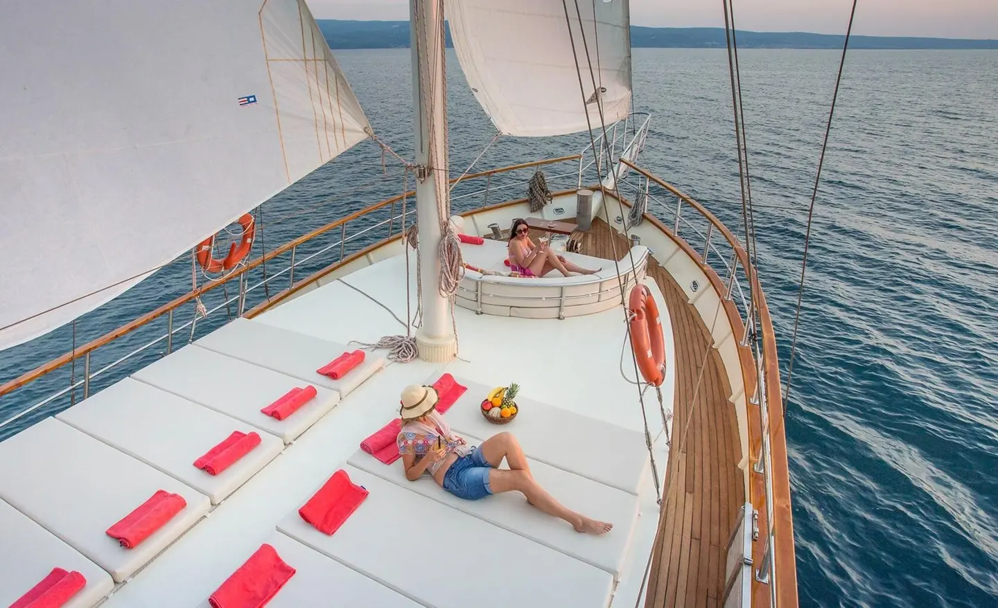 Altair yacht on calm sea at sunset, white deck, red cushions, open bow