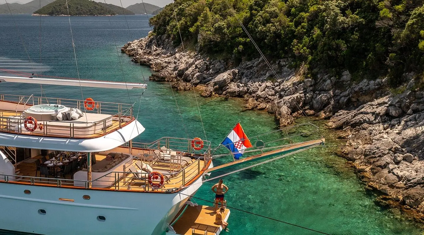 Love Story yacht anchored near rocky coastline with small boats nearby