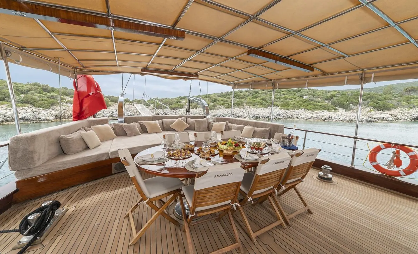 Arabella yacht deck seating area with wooden chairs and a table under a shaded canopy