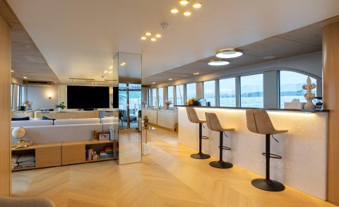 Luxurious yacht interior with a seating area and white bar counter with stools, large windows showing the outside view