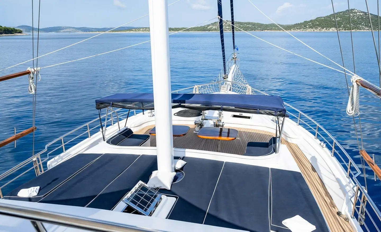 Aurum yacht deck at sunset with wooden seating, sailboat rigging, calm blue sea