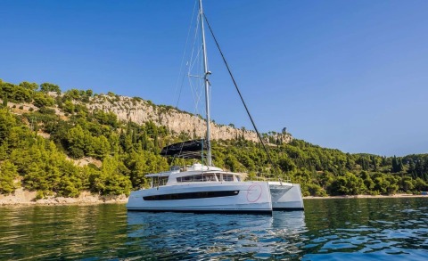 Catamaran sailing yacht on calm water with rocky forested coastline