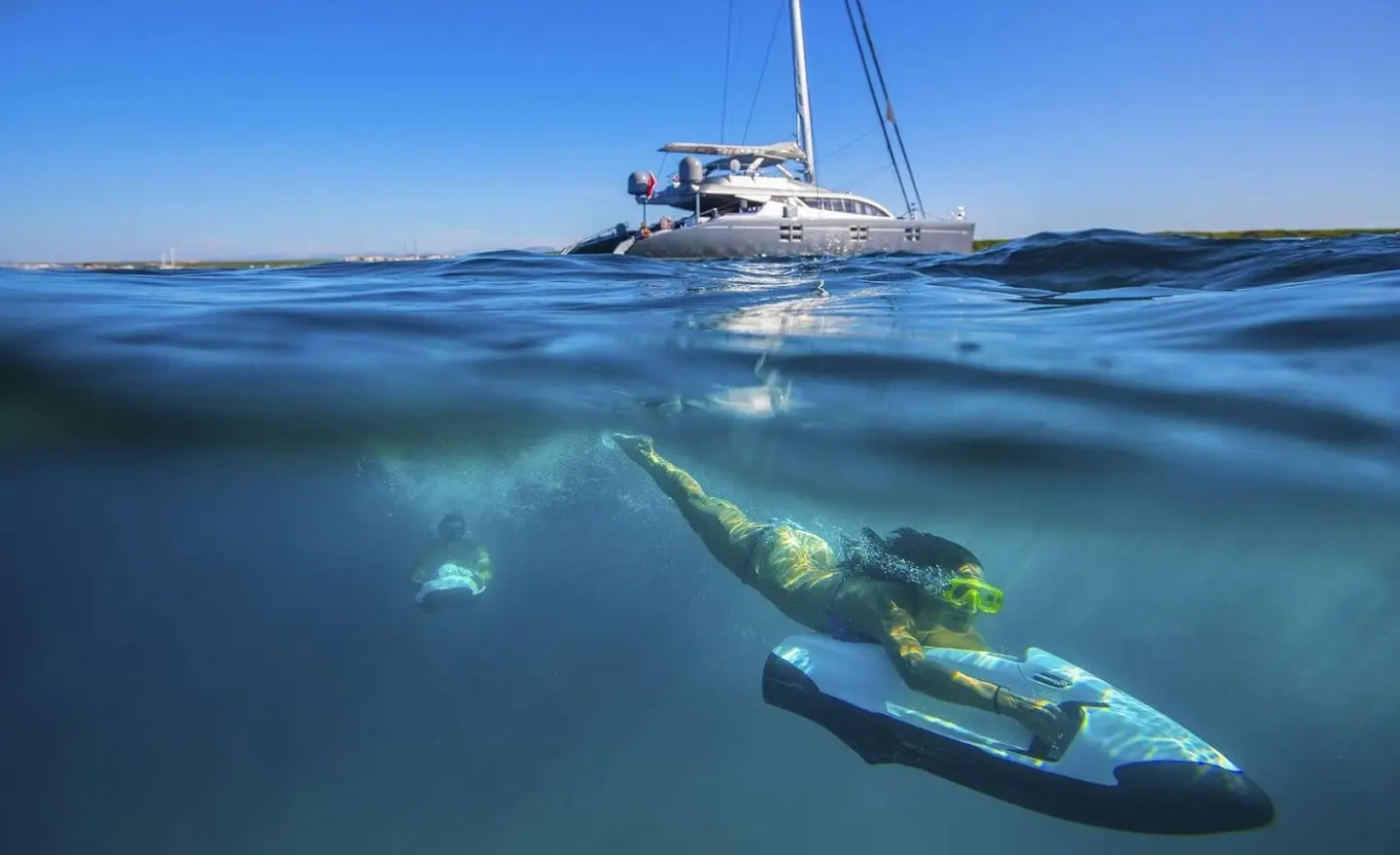 Underwater: snorkeler explores clear blue water near a luxury motor yacht named Cartouche
