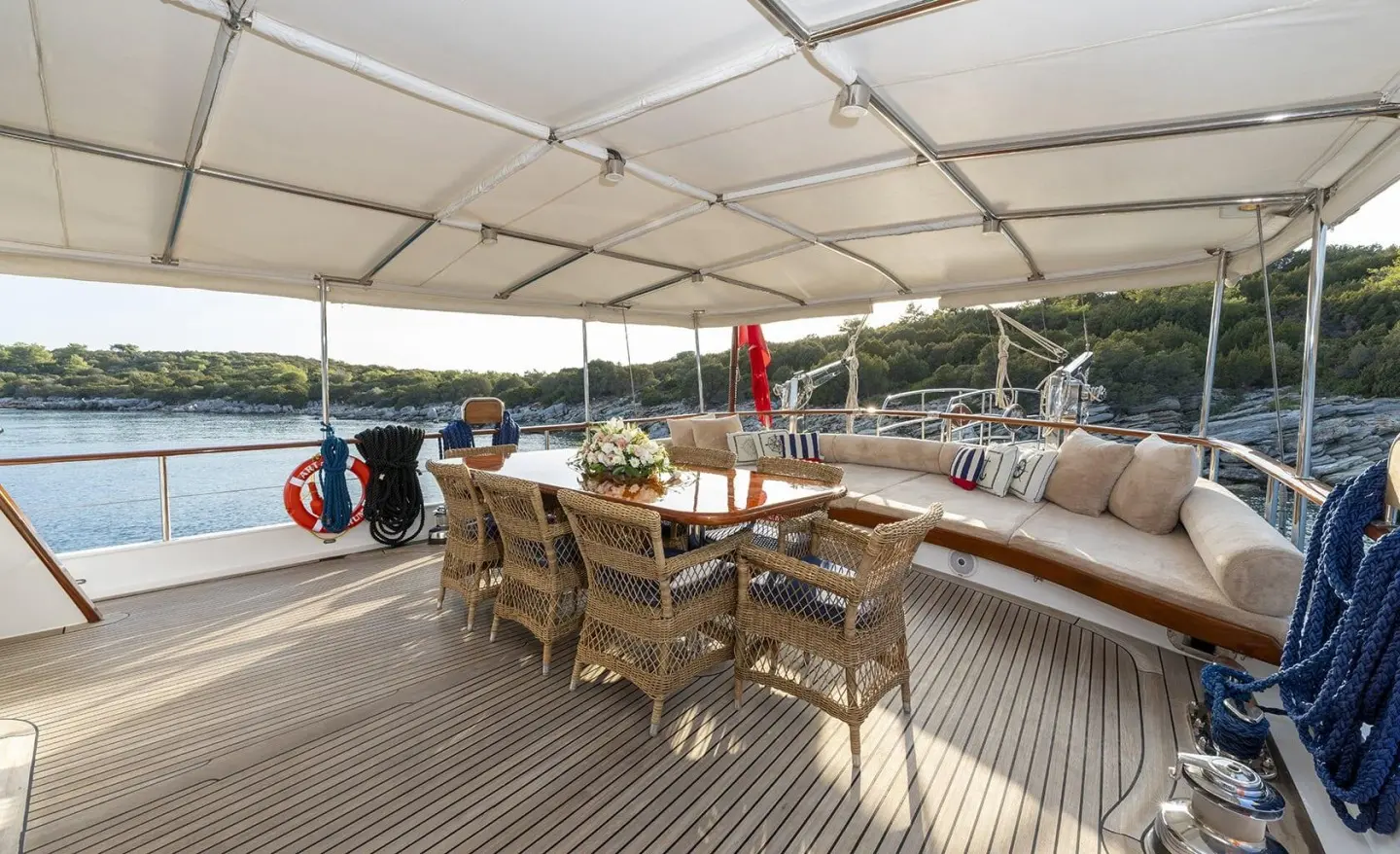 Artemis yacht deck with wooden table, chairs, and shaded seating area at sunset