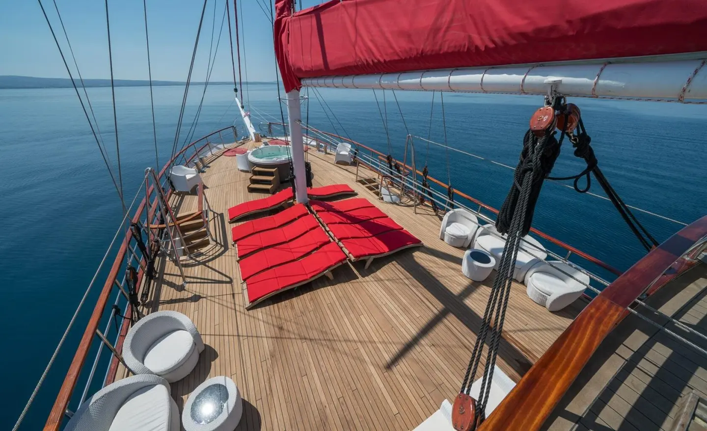 View of the Barbara yacht deck with red cushions, winches, and blue sea backdrop