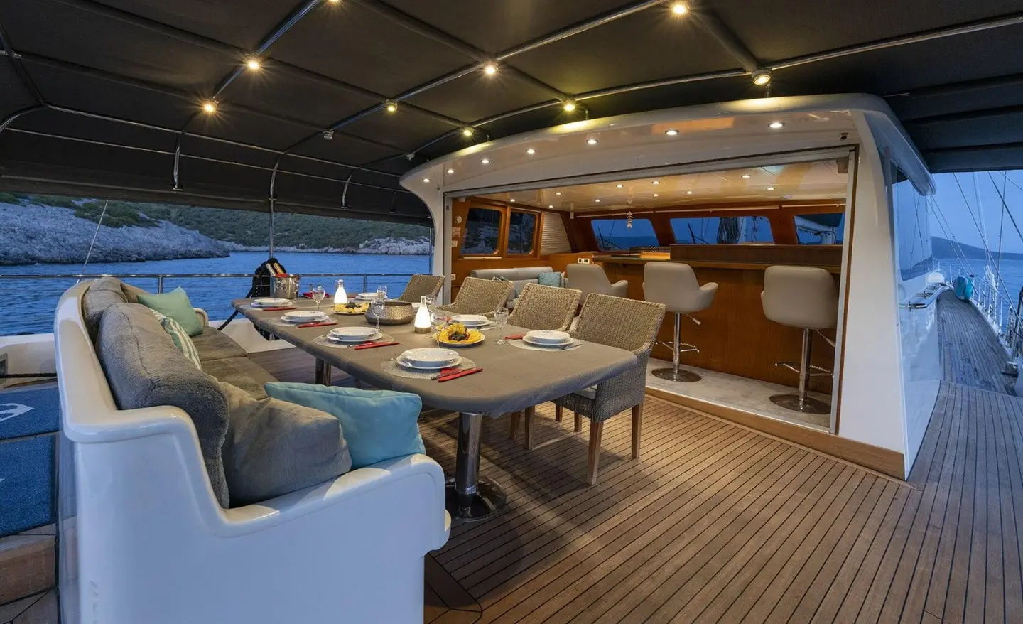 Yacht Lucky You deck dining area with chairs, table, and string lights at sunset