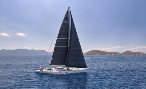 Aizu yacht with large dark sails on the open sea, white hull sailing view