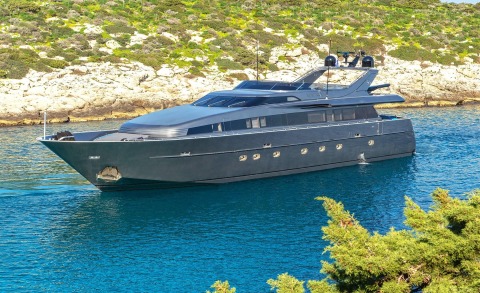 Dark blue motor yacht Summer Fun anchored in clear blue water near rocky shore