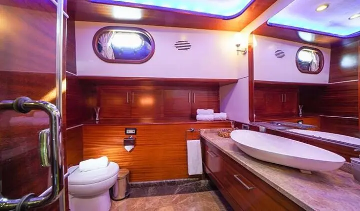Luxurious yacht cabin with wooden cabinetry, porthole, bed, and ensuite bathroom vanity