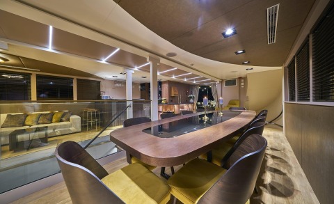 Interior of Rara Avis yacht: wooden dining table with chairs, modern lighting, and glass railing in the salon