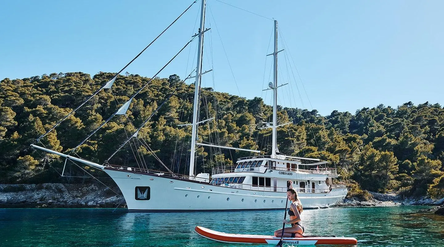 Corsario yacht with white hull anchored near rocky coastline under clear blue sky