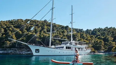 Corsario yacht with white hull anchored near rocky coastline under clear blue sky