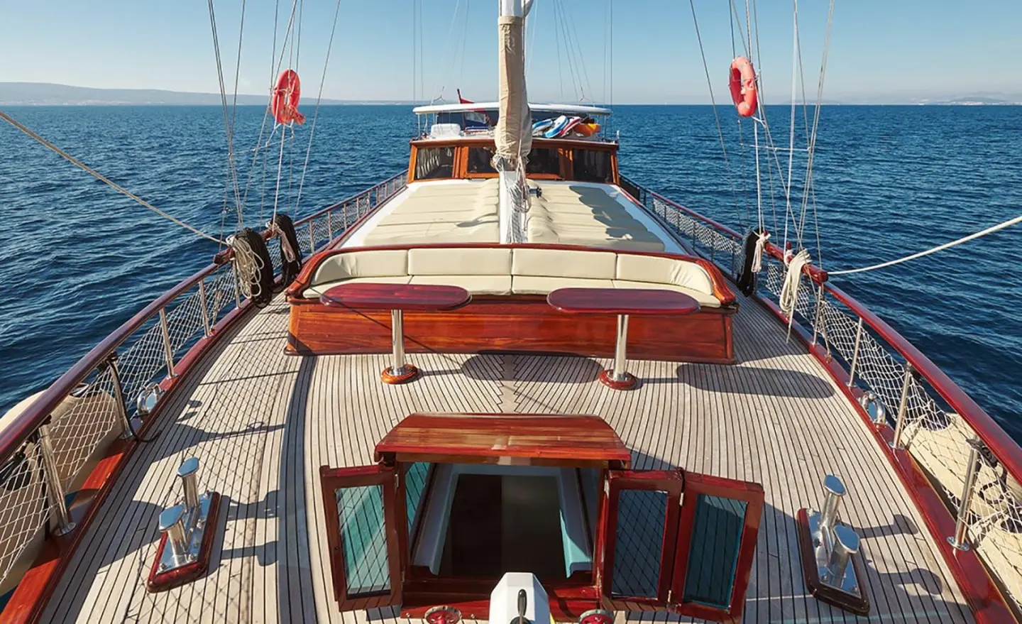 Linda yacht deck view with sunlit teak and red-cushioned seating on stern