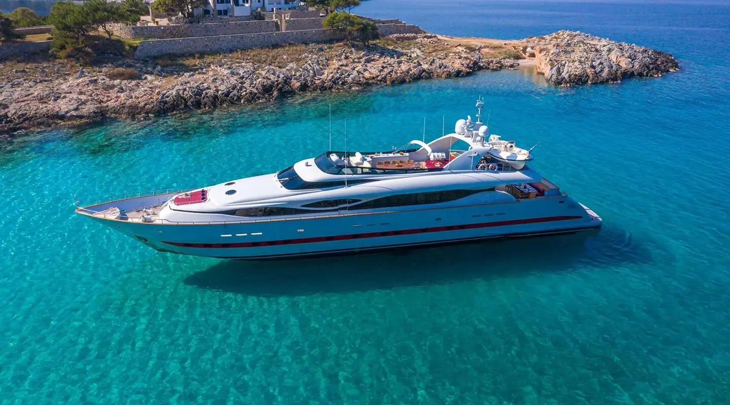 Glaros luxury yacht anchored in turquoise coastal waters, rocky shoreline visible