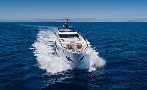 White luxury motor yacht cutting through blue sea with open deck and seating area at bow