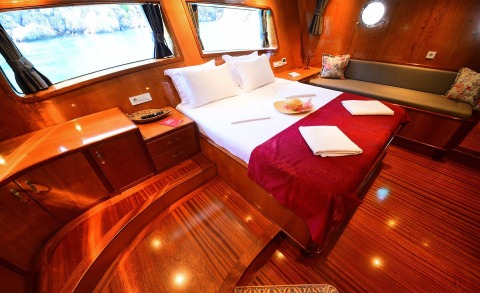 Maya yacht master cabin with white sheets, red throw, wooden cabinetry and windows