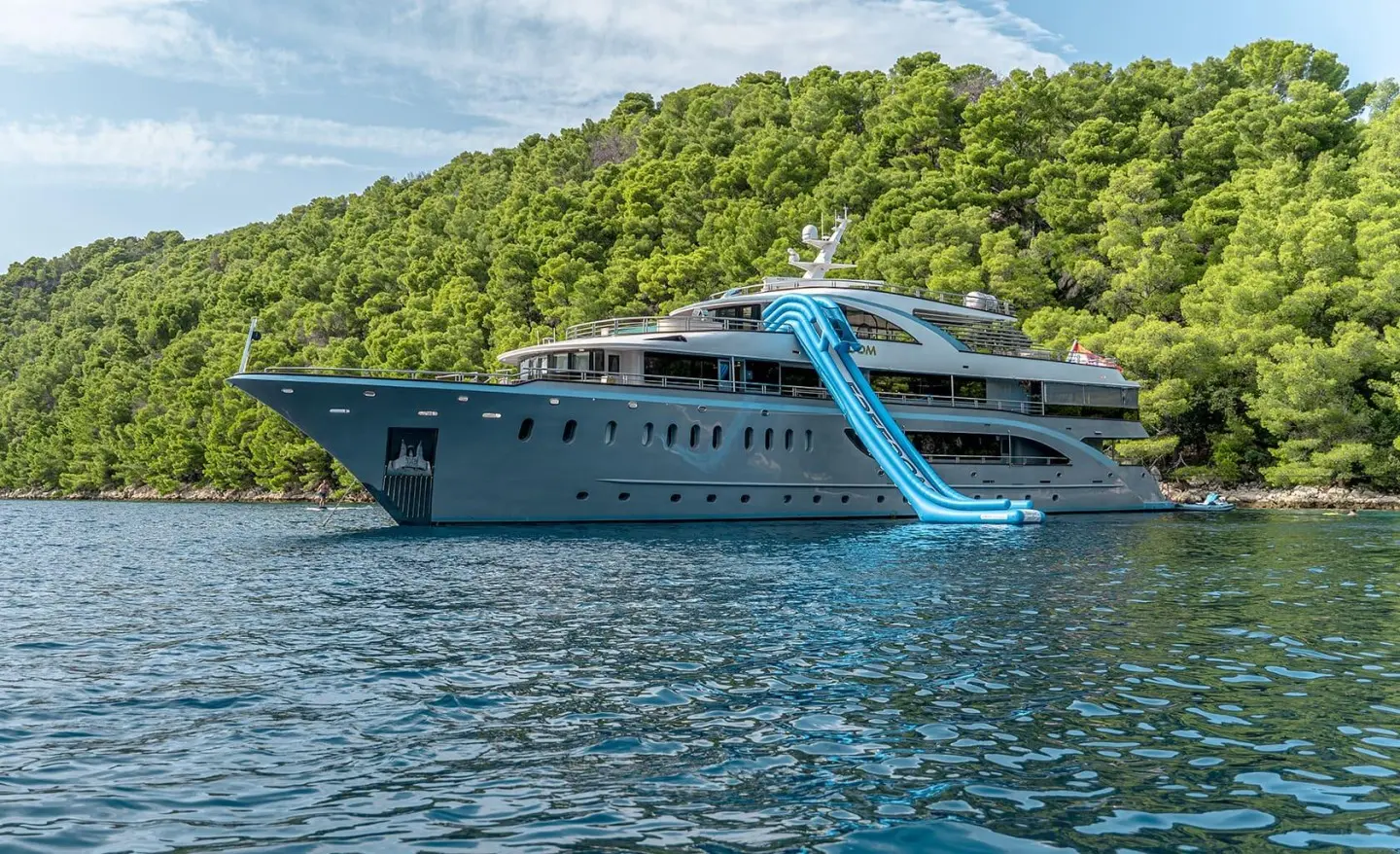 Blue motor yacht with a large water slide along the side and multiple decks