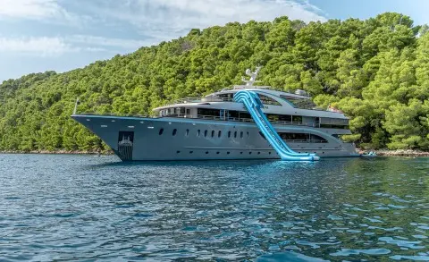 Blue motor yacht with a large water slide along the side and multiple decks