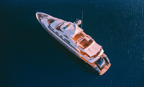 White luxury yacht seen from above, deck area with sun loungers and canopy on blue sea