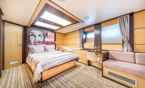 Hotel-like yacht cabin with large bed, art piece above, desk, curved headboard, and wood-paneled walls