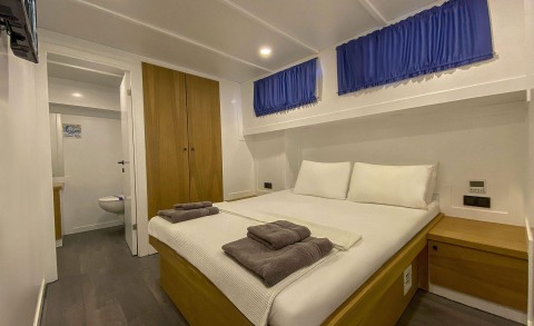Interior of a cabin with a large bed, wooden wardrobe, and blue curtains in a yacht
