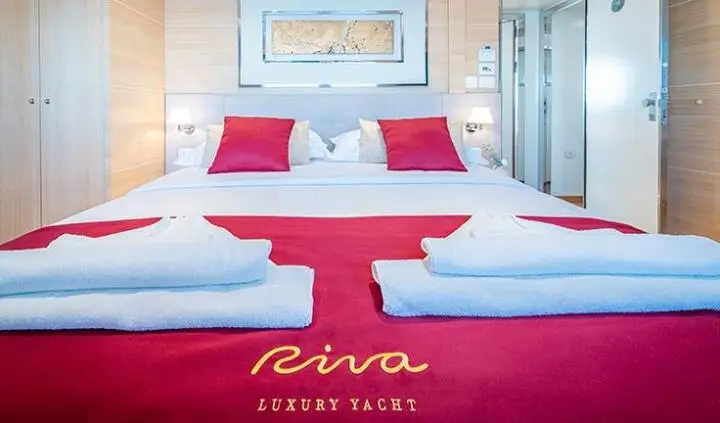 Master cabin with two large beds, white linens, red bed runner, wooden flooring