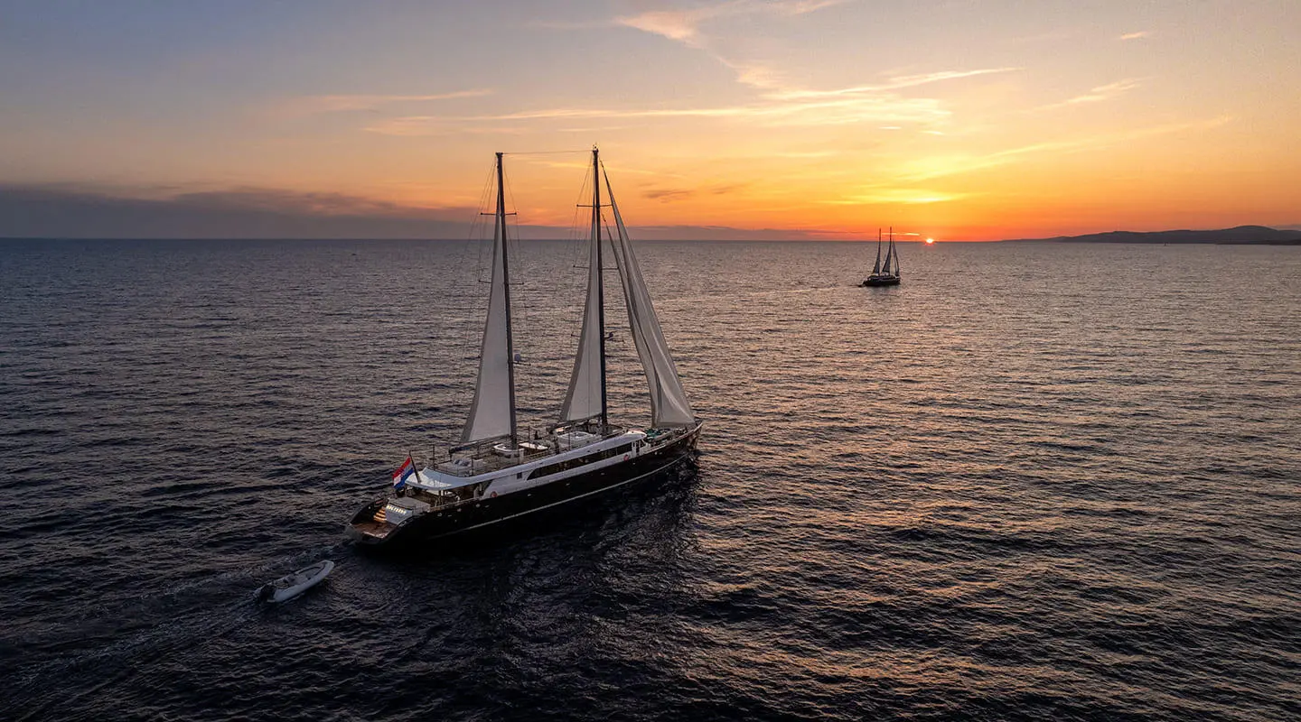 Two-masted large yacht at sunset on open sea with a small motor yacht nearby