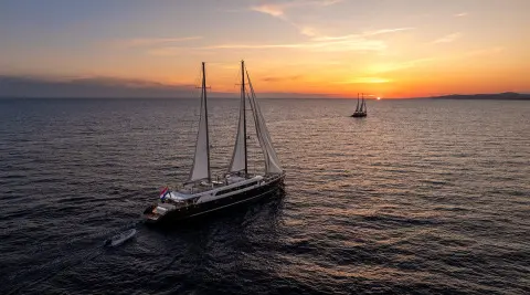 Two-masted large yacht at sunset on open sea with a small motor yacht nearby