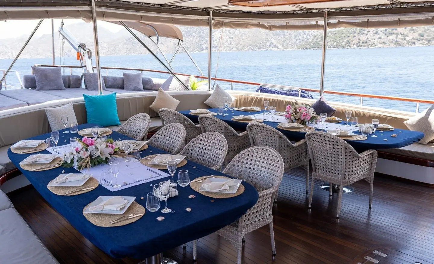 Aft deck of Nevra Queen gulet with blue tablecloths and cushioned seating on a sunny day
