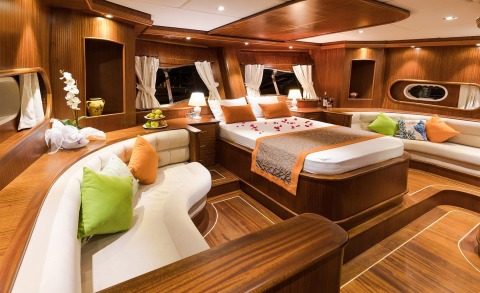 Interior of Vista Mare luxury yacht cabin with wooden panels, large bed with pillows, seating area, windows and lamps
