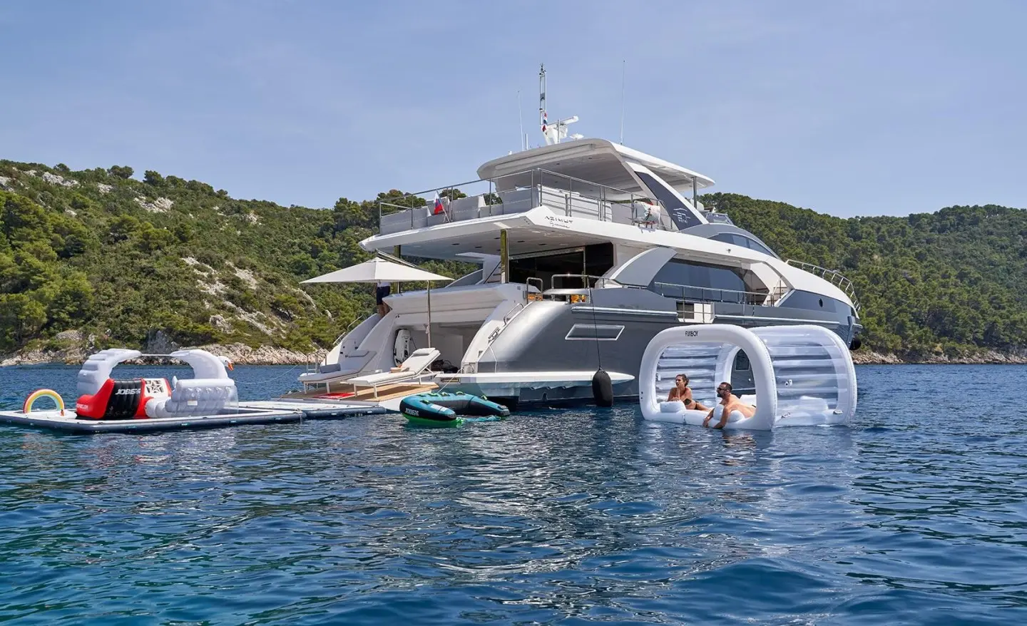 Large white motor yacht anchored near rocky shoreline with water toys nearby