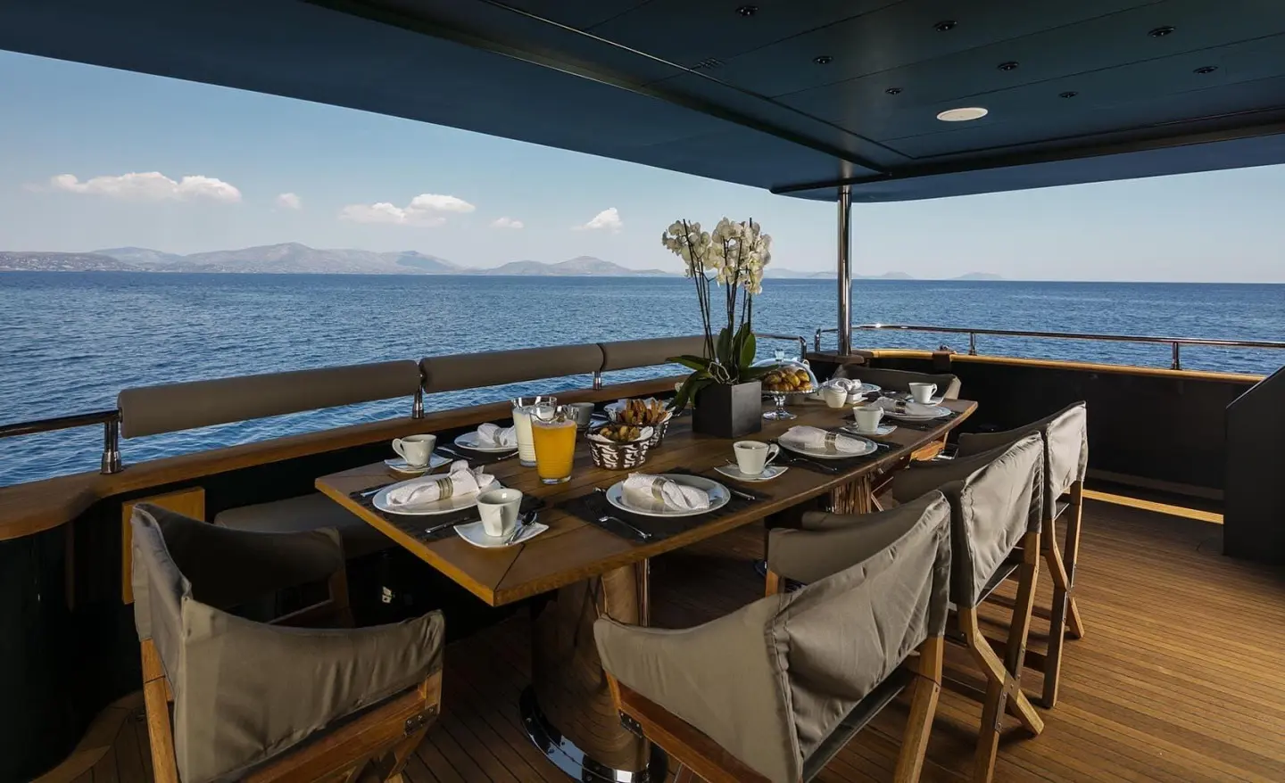 Elegant yacht dining setup on deck at sunset with tableware and chairs