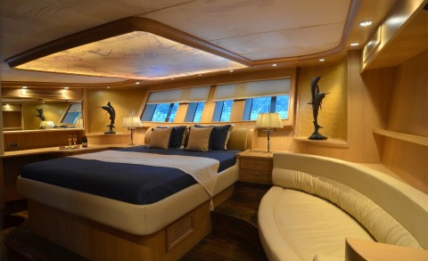 Master bedroom on a wooden yacht interior with windows, bedside lamps and a curved cream sofa