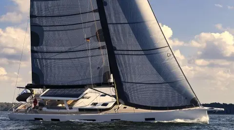 Nadamas motor yacht sailing with large dark sails against blue sky