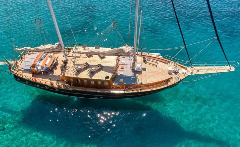 Wooden-decked yacht with seating area and sails on clear blue water