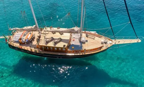 Wooden-decked yacht with seating area and sails on clear blue water