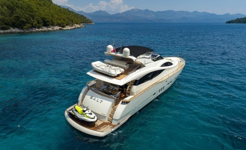 White luxury yacht on blue sea with open upper deck seating area and watercraft on stern under sunset