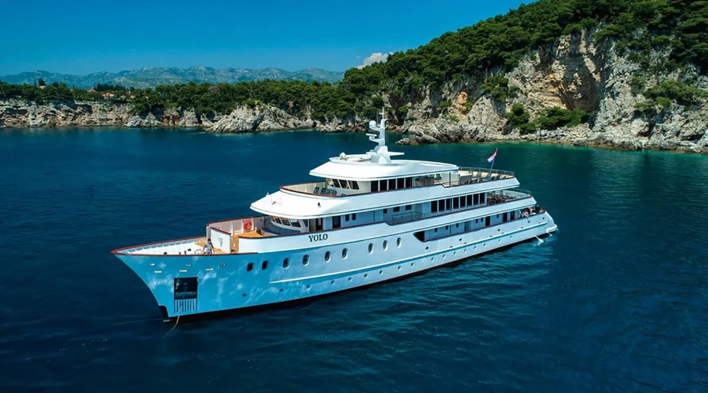 YOLO yacht anchored in blue water near rocky coastline.