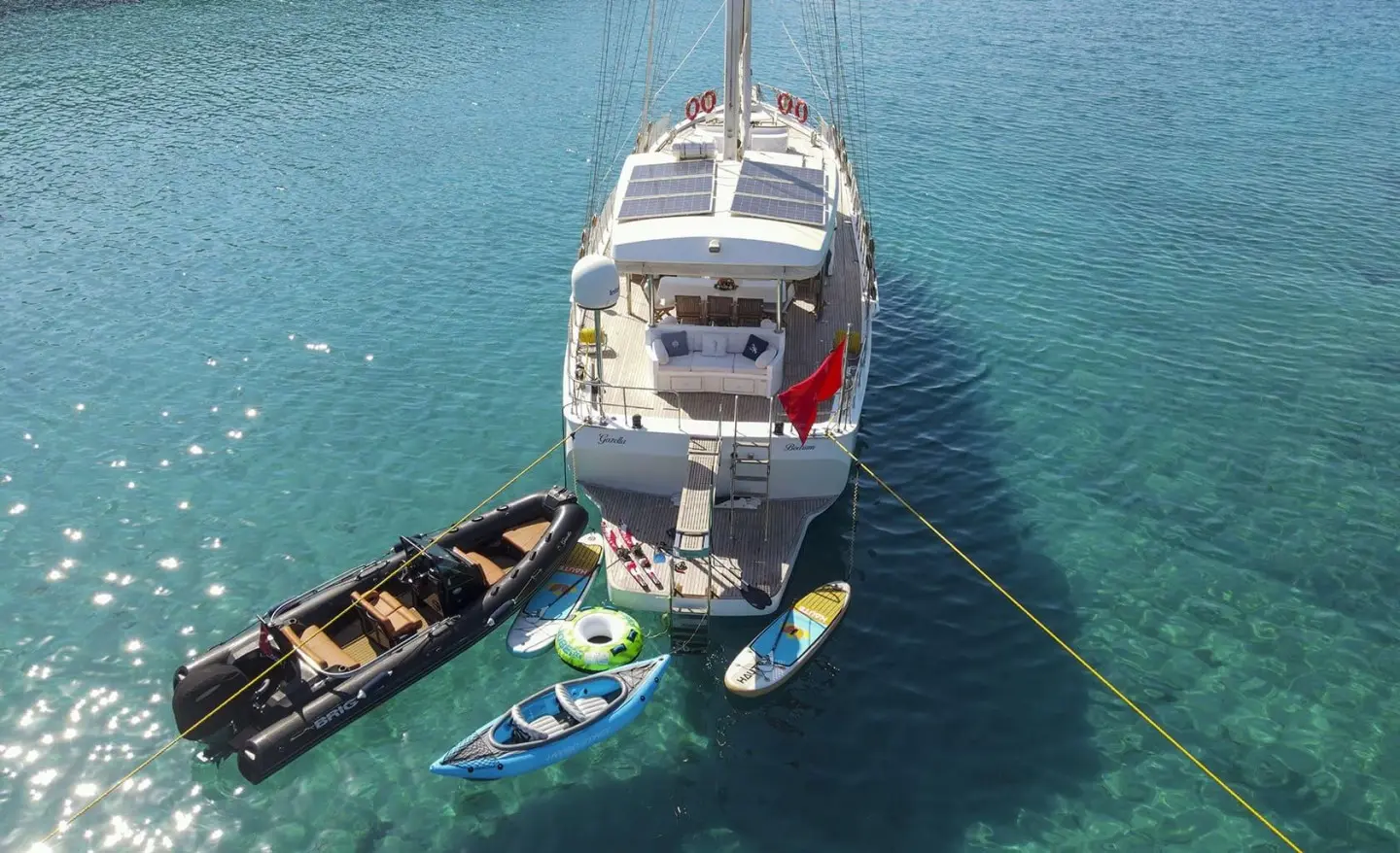 Gazella yacht anchored with two small boats nearby on calm blue water at sunset