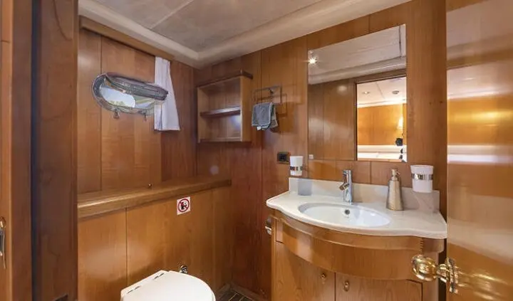 Wooden cabin interior with berth, sink, mirror, and porthole on Queen Of Sea