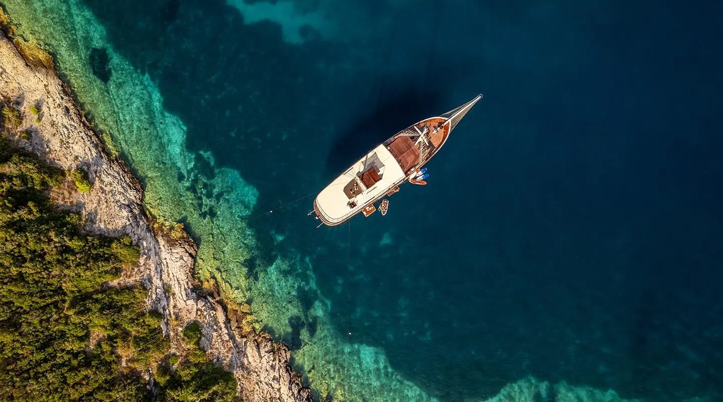Cesarica yacht anchored in clear turquoise water near rocky coastline at sunset